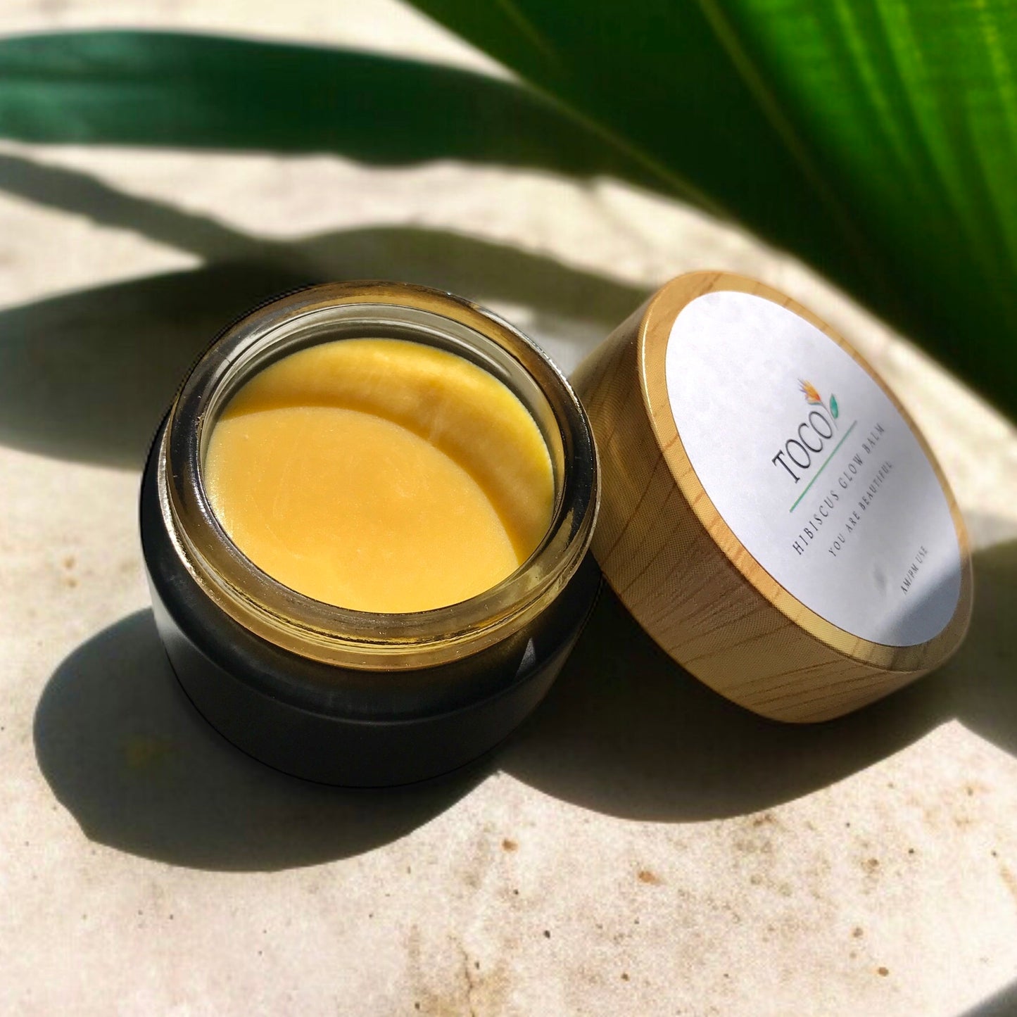 open black glass jar and lid of hibiscus glow balm in sunlight