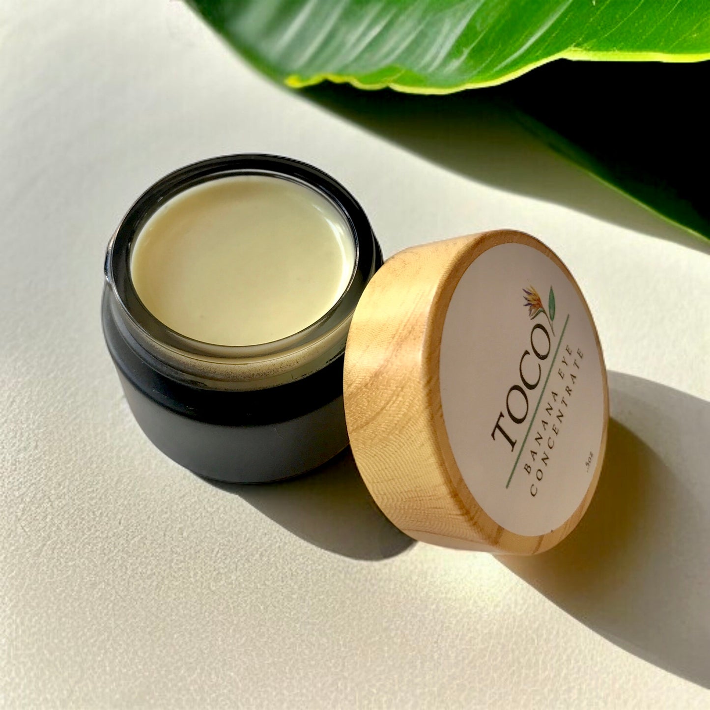 Banana Eye Concentrate in black jar with a green leaf in background