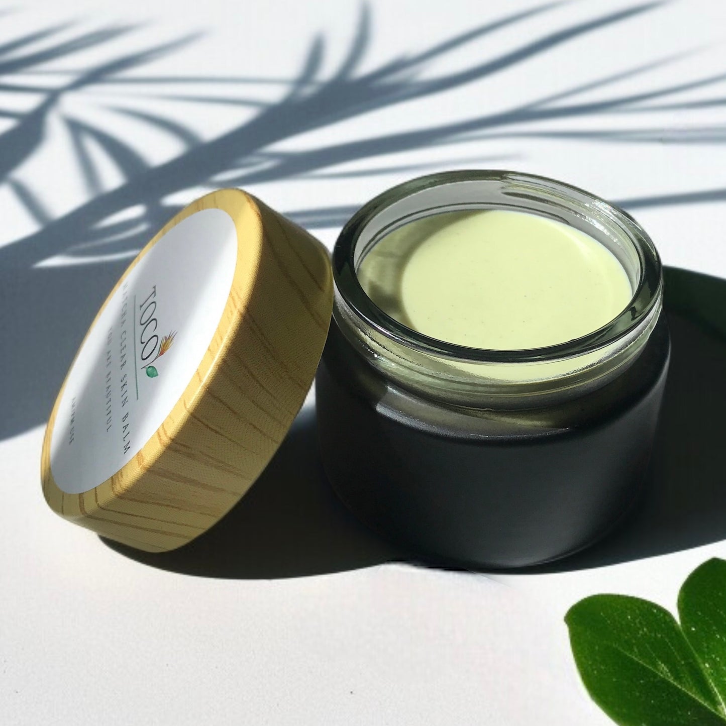 Open jar of Matcha Clear Skin Balm with a  lid on a white background