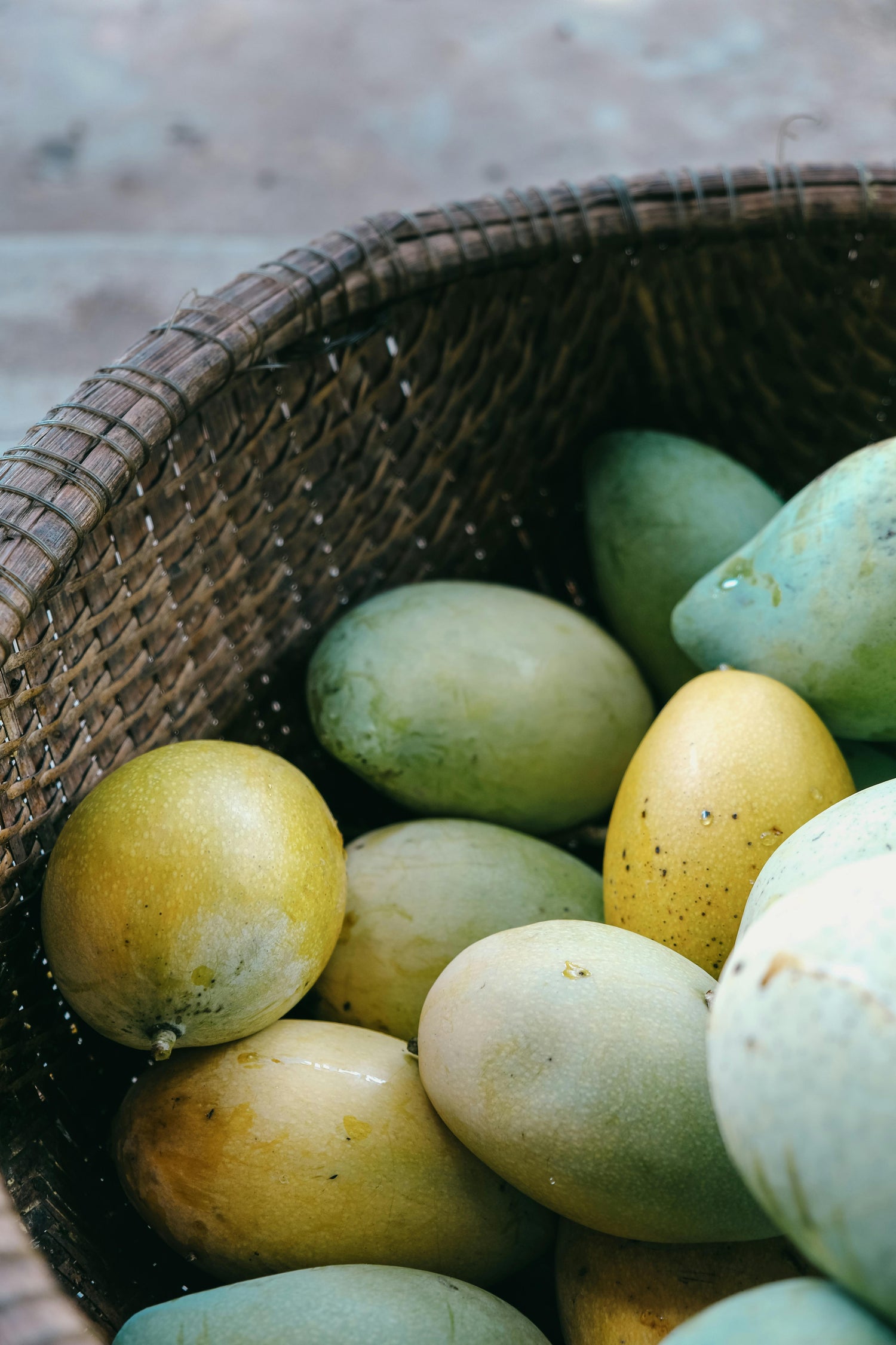 Basket filled with green and yellow mangoes on a textured surface