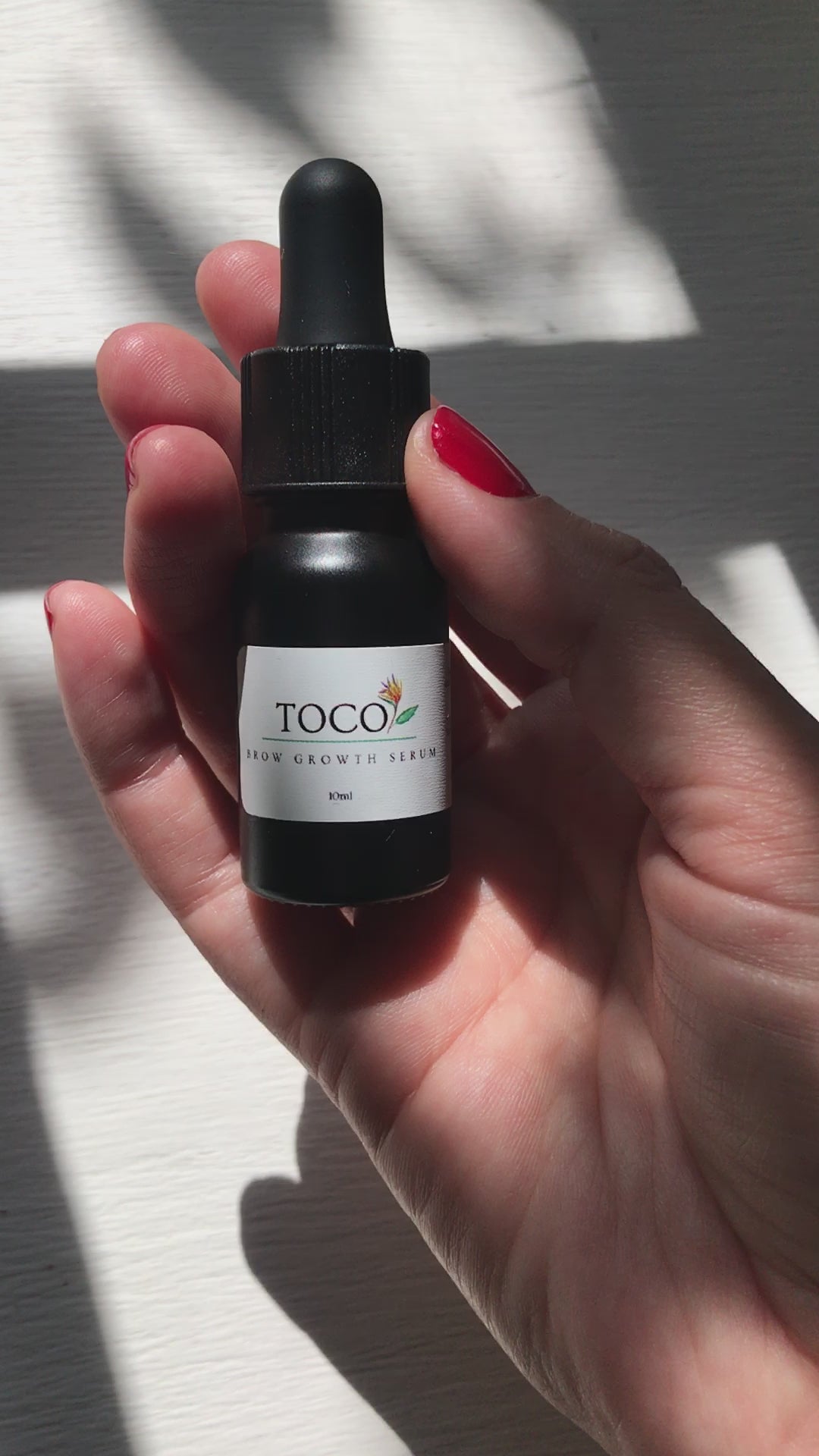 10ml black glass dropper bottle of brow growth serum being poured into hand in sunlight 