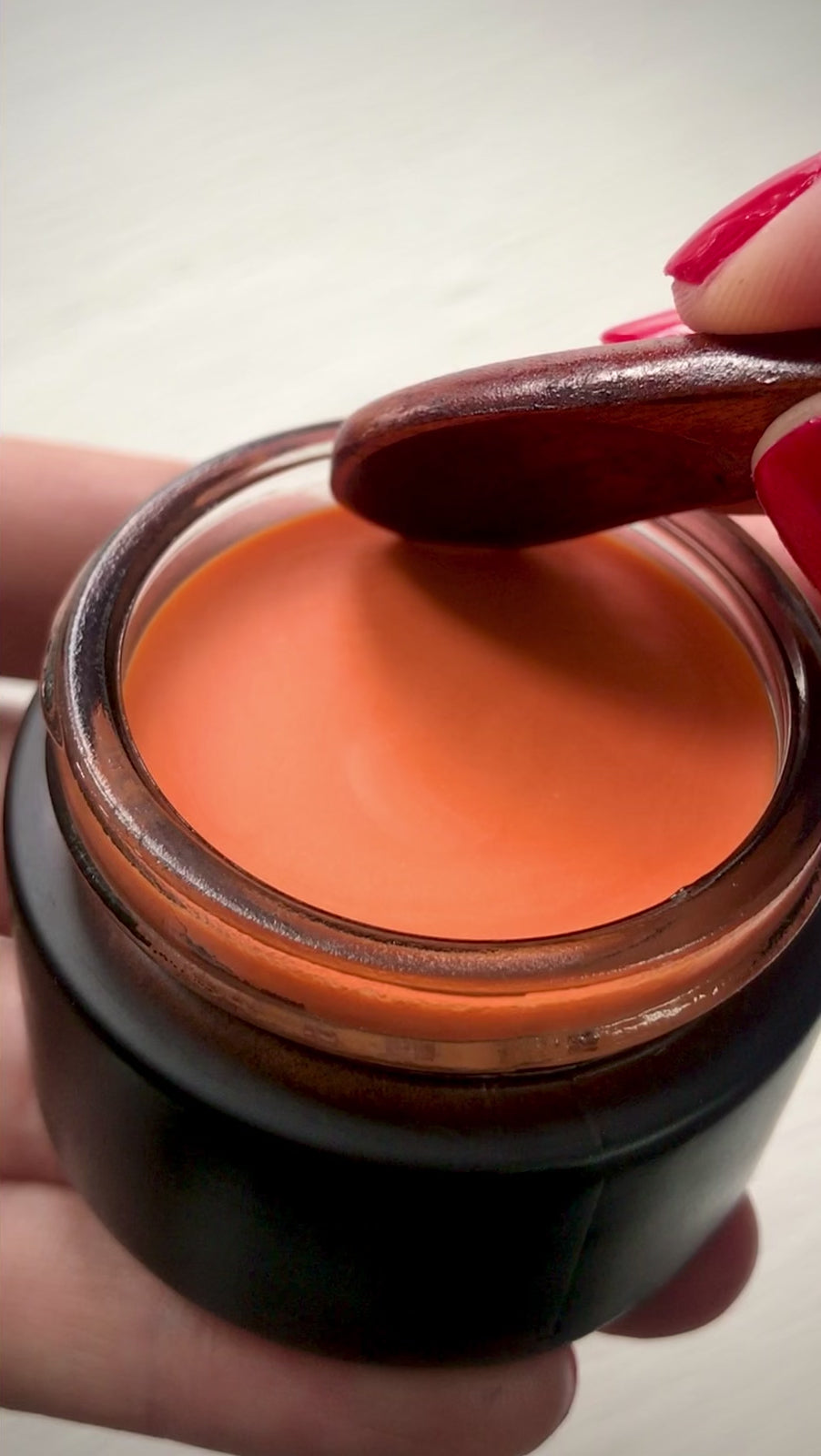 Scooping Hibiscus glow balm with wooden spoon