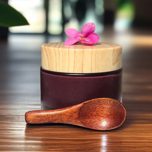 rose petal and clay exfoliator in a  glass jar next to small wooden spoon